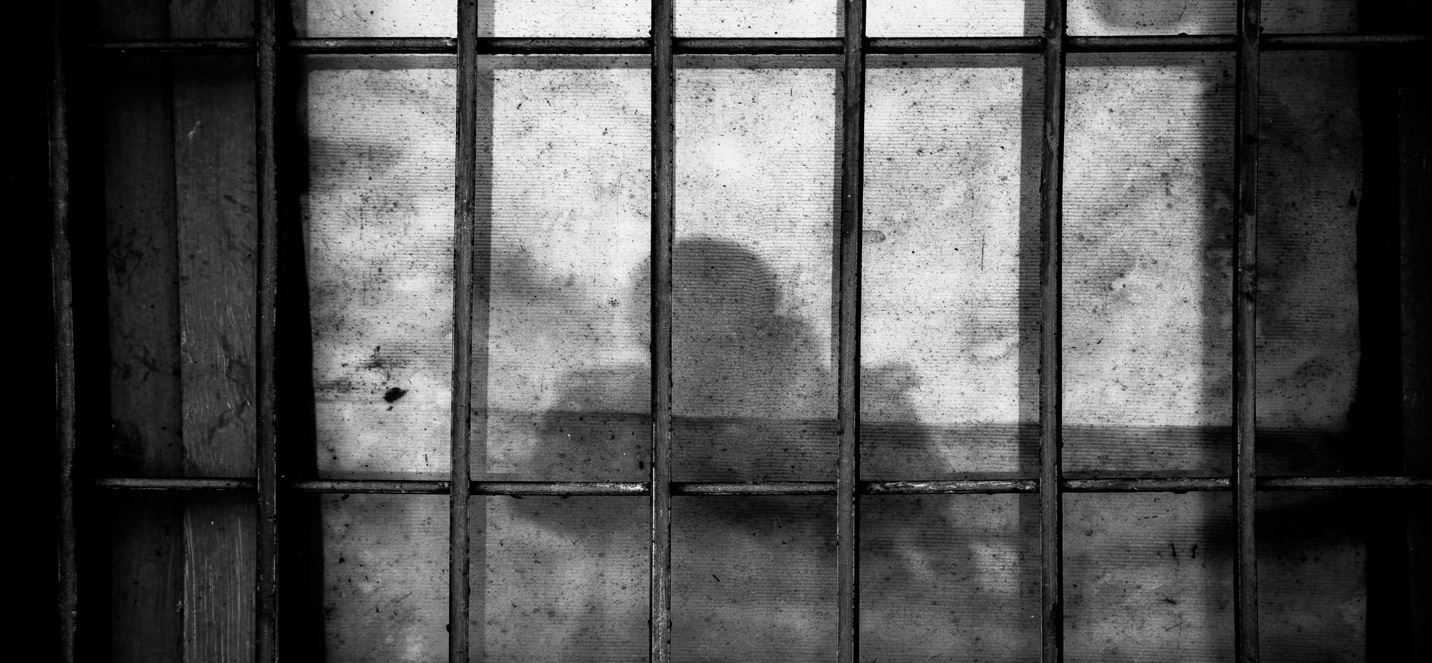 A shadow of a person behind bars

Description automatically generated